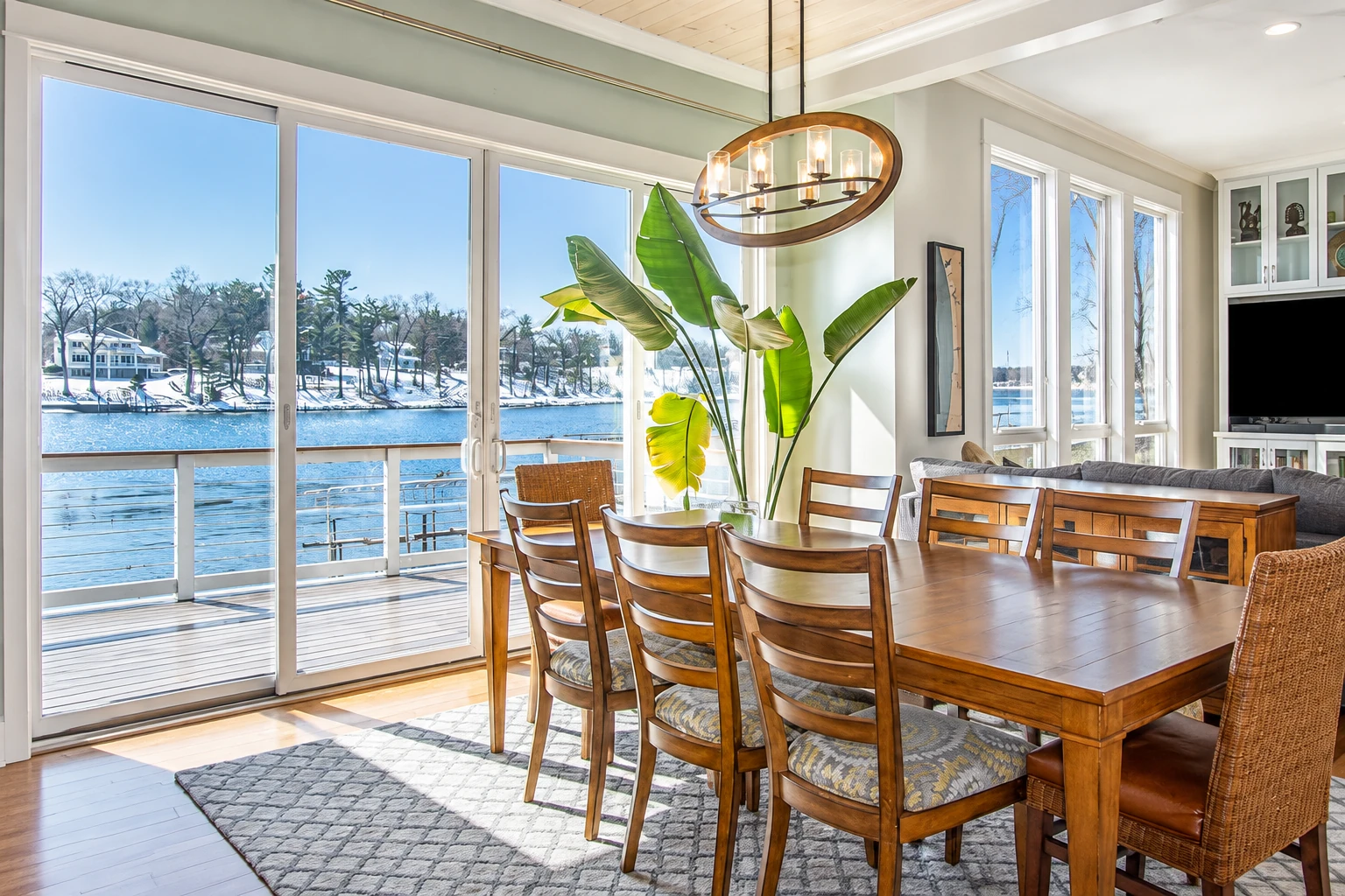 Sunroom dining area with a wooden table, large windows, and a snowy waterfront view.