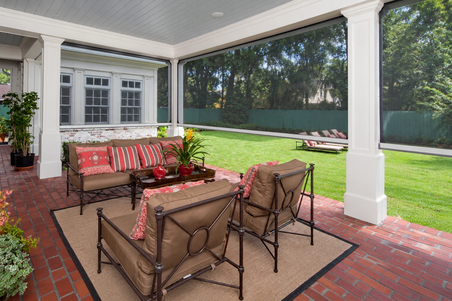 Screened patio room with white columns, a brick floor, and cushioned seating beside a green lawn.